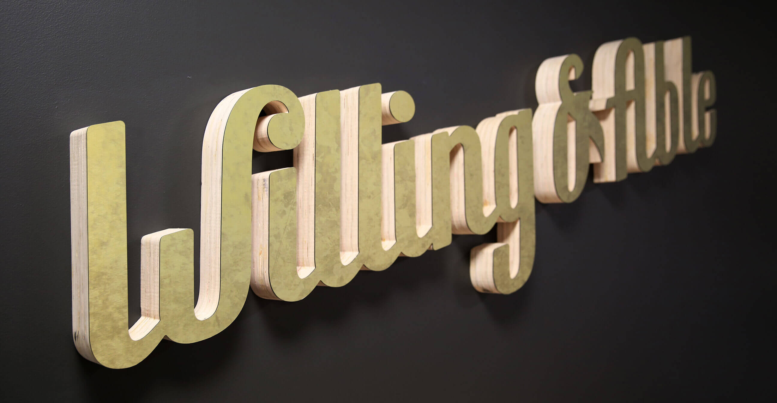 3D wall sign with the words Willing & Able in large, cursive gold letters mounted on a dark background.
