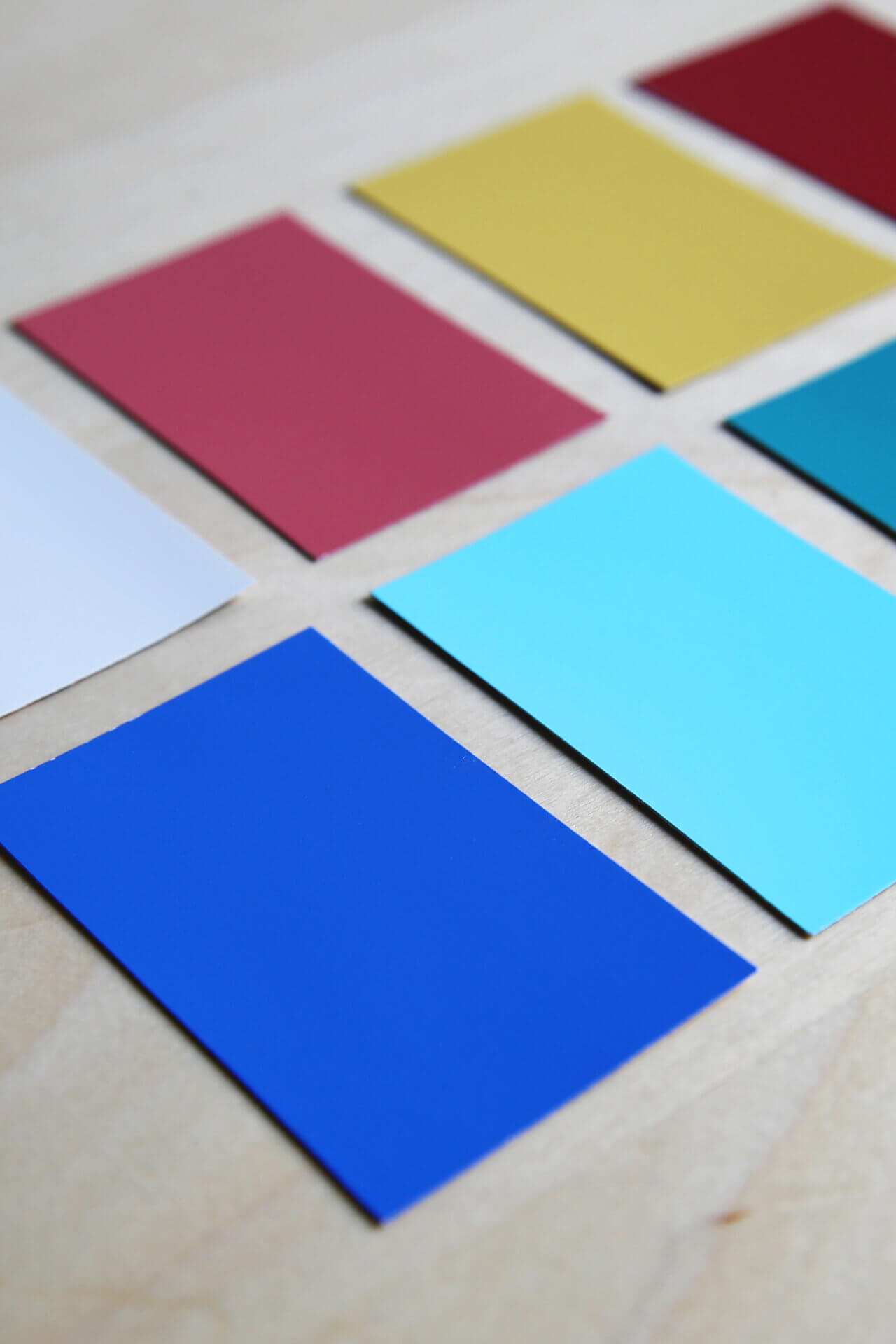 Rectangular color swatches in shades of blue, red, yellow, white, teal, and light blue are arranged in neat rows on a light wooden surface.