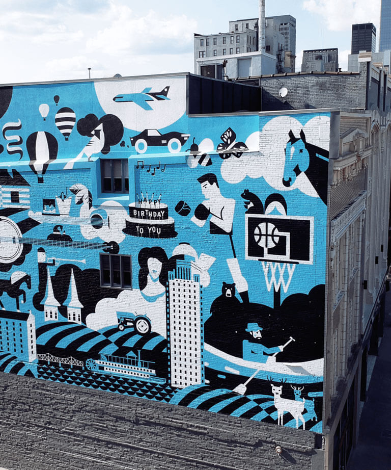 A vibrant mural on a city building features various black and white illustrations on a blue background, including a boxer, basketball hoop, guitar, animals, buildings, and musical notes, creating an energetic urban scene.