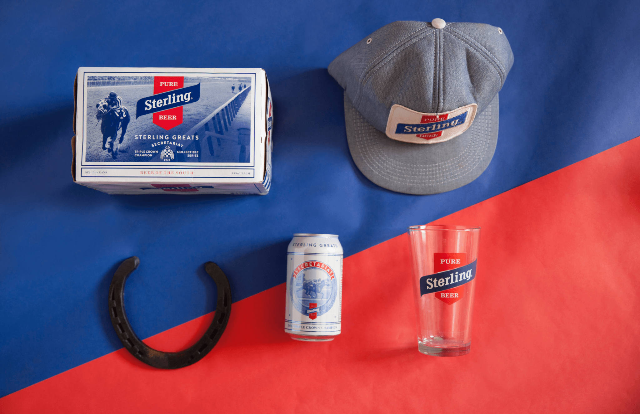 A Sterling beer box, can, glass, grey cap, and a horseshoe are arranged on a blue and red background. All items are branded with the Sterling logo.
