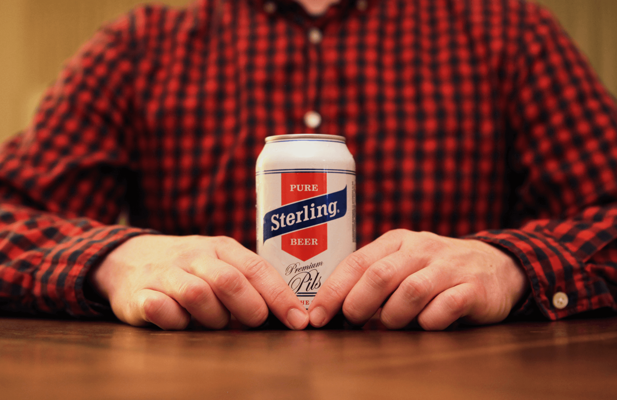man with plaid shirt holding sterling beer
