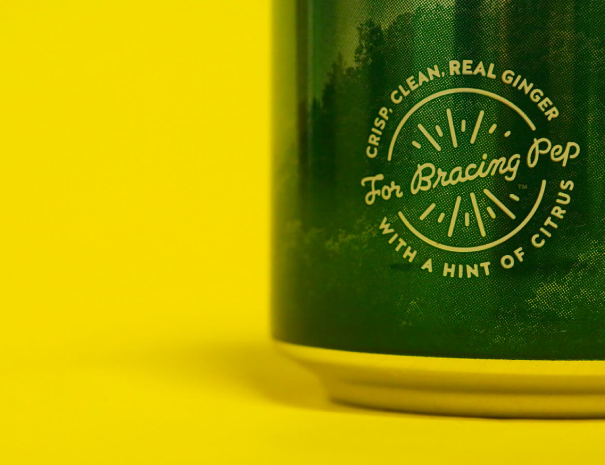 A close-up of a green beverage can against a bright yellow background. The cans label reads CRISP. CLEAN. REAL GINGER For Bracing Pep WITH A HINT OF CITRUS in white letters.