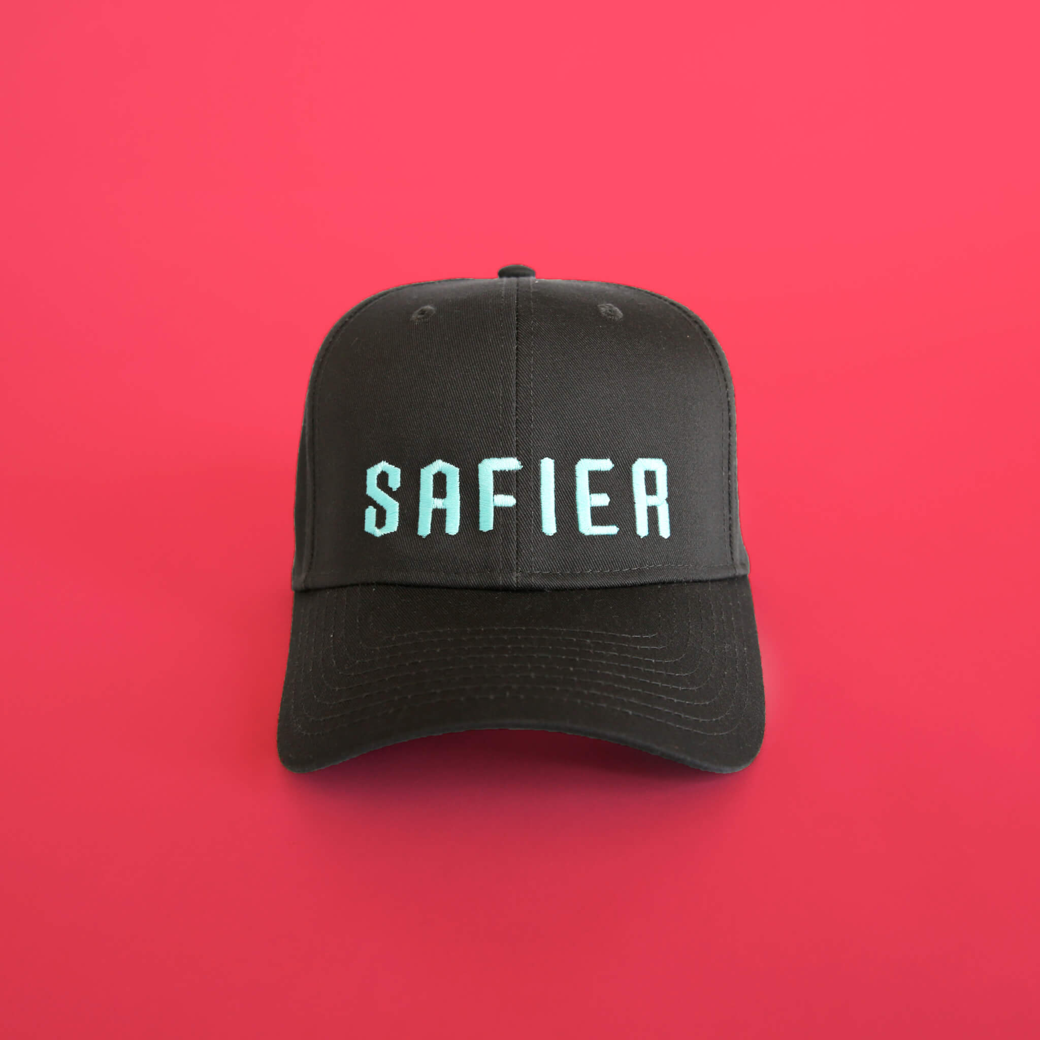 A black baseball cap with the word SAFIER in light blue capital letters on the front, displayed against a solid bright pink background.