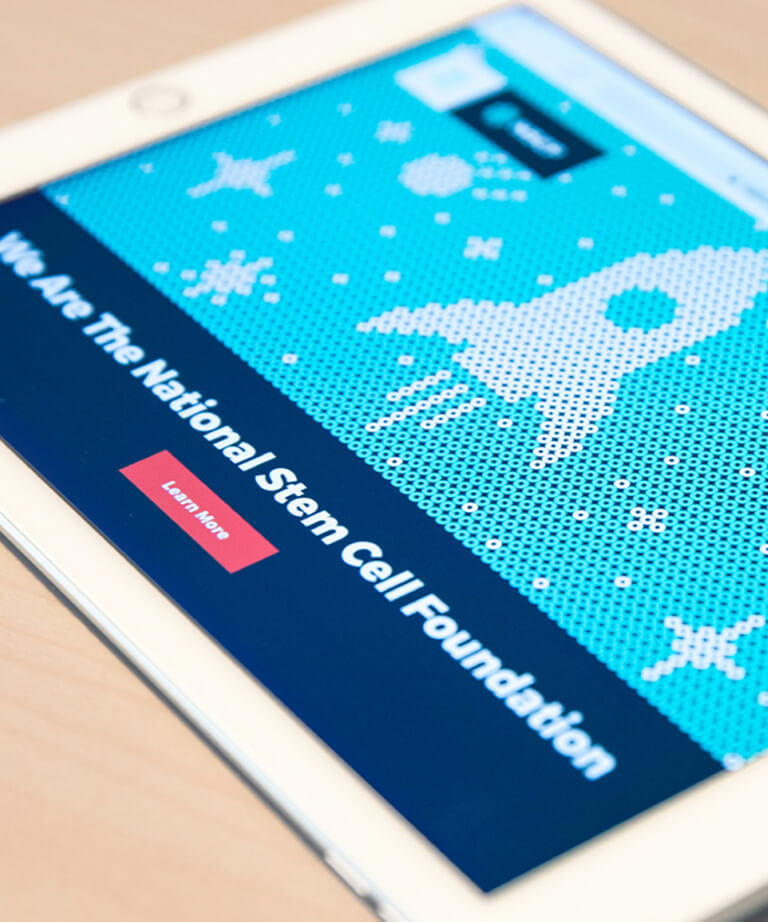 A tablet screen displays the National Stem Cell Foundation website, featuring a blue background with white pixelated space-themed graphics, including a rocket and stars, and a Learn More button.