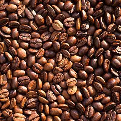 A close-up view of many roasted coffee beans, showing their rich brown color and shiny surface, tightly packed together and filling the entire frame.