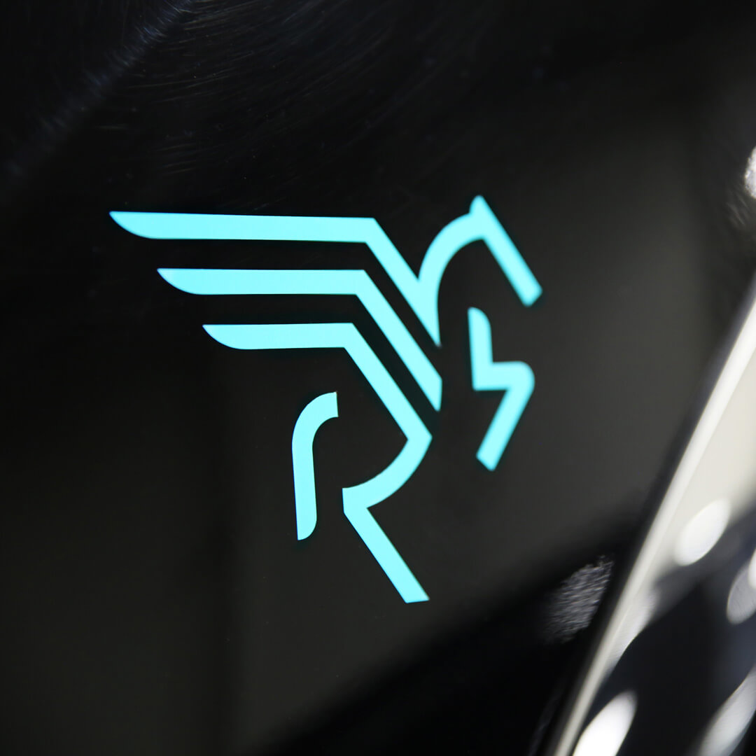 A close-up of a stylized turquoise logo resembling a winged horse with the letters RS on a glossy black surface.