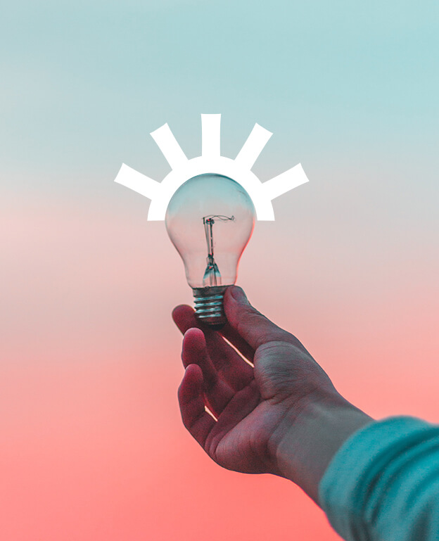 A hand holds a clear light bulb against a pink and blue gradient sky. White graphic lines above the bulb resemble rays, giving the appearance of a shining or illuminated light bulb.