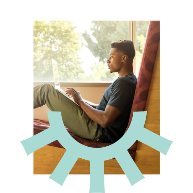 A young man sits in a cozy window seat, working on a laptop. Sunlight streams through the window, and a light blue abstract graphic overlays the bottom of the image.