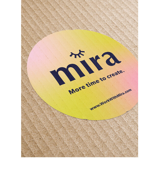A round, yellow-pink gradient sticker on a ribbed brown surface displays the text mira with an eye illustration and the slogan More time to create. The website www.WorkWithMira.com appears at the bottom.