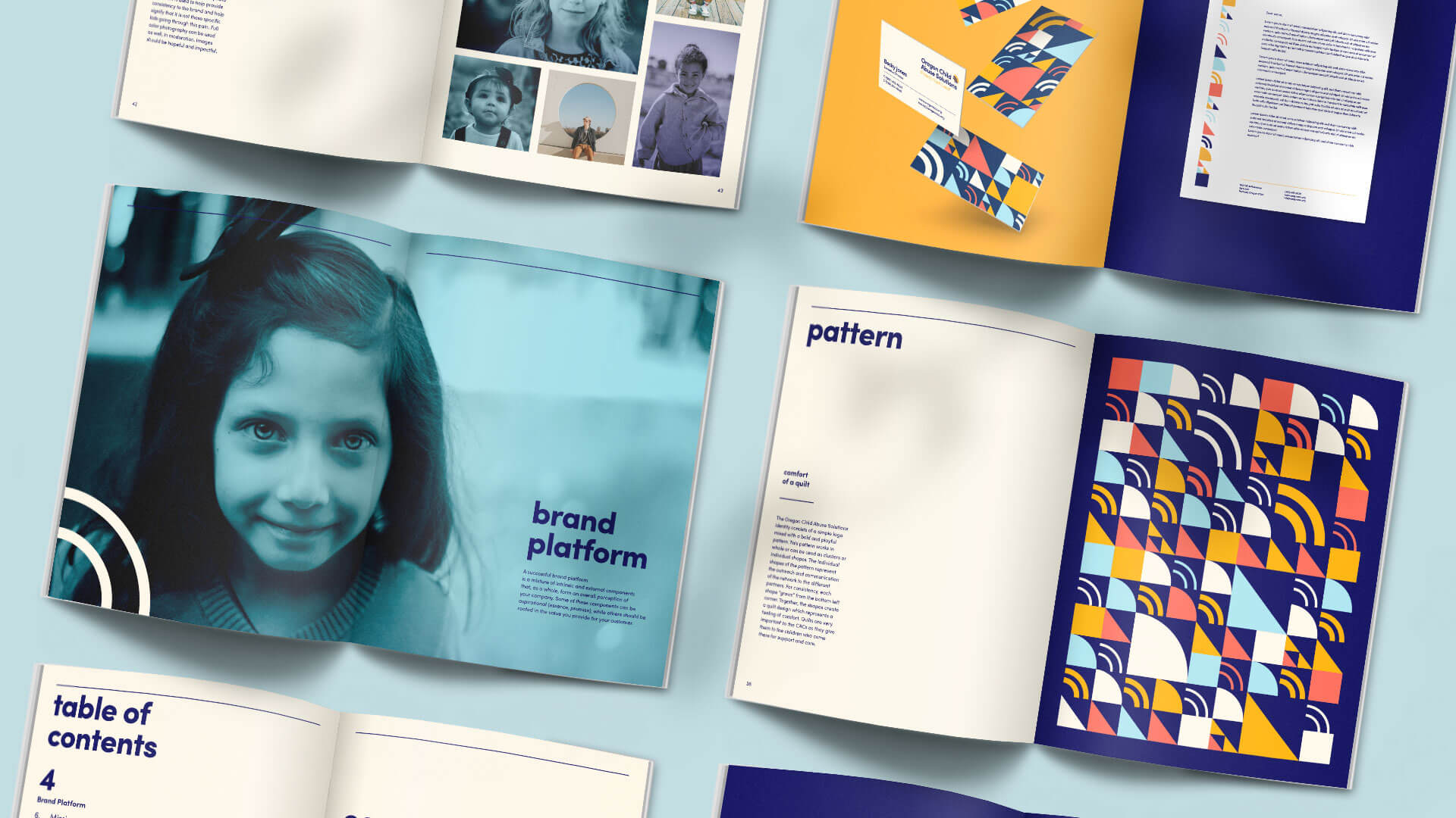 Several open brand guidelines booklets are laid out on a light surface. Pages feature colorful geometric patterns, a blue-tinted photo of a smiling girl, and sections on brand platform, pattern, and table of contents.