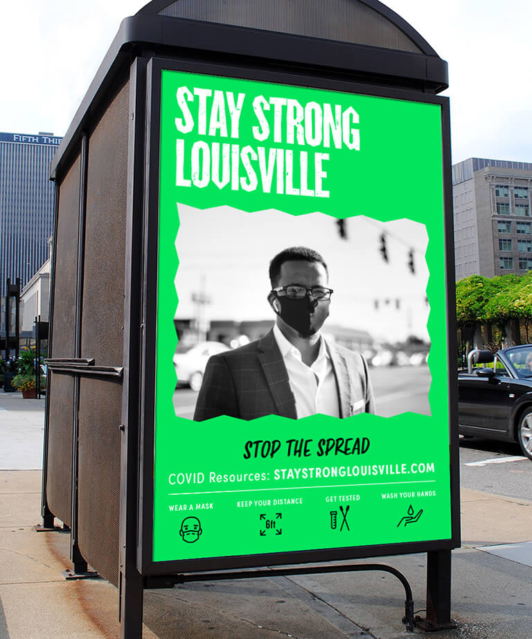 A city bus stop ad features a man in a suit and face mask with the text “Stay Strong Louisville. Stop the Spread” and COVID-19 safety tips: wear a mask, keep distance, get tested, and wash hands.