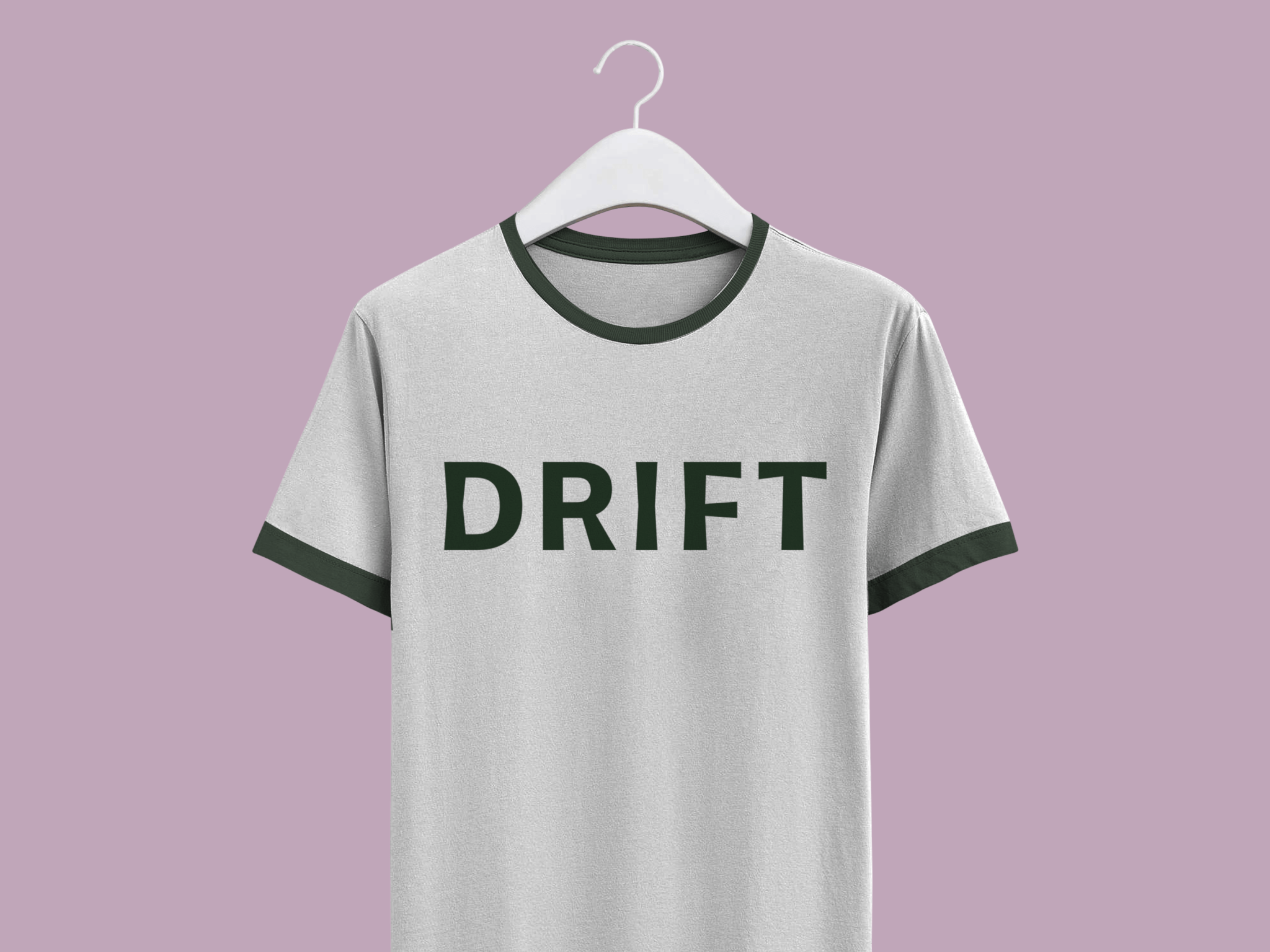 A light gray t-shirt with black collar and sleeve edges hangs on a white hanger against a lavender background. The word DRIFT is printed in bold black letters on the shirts front.