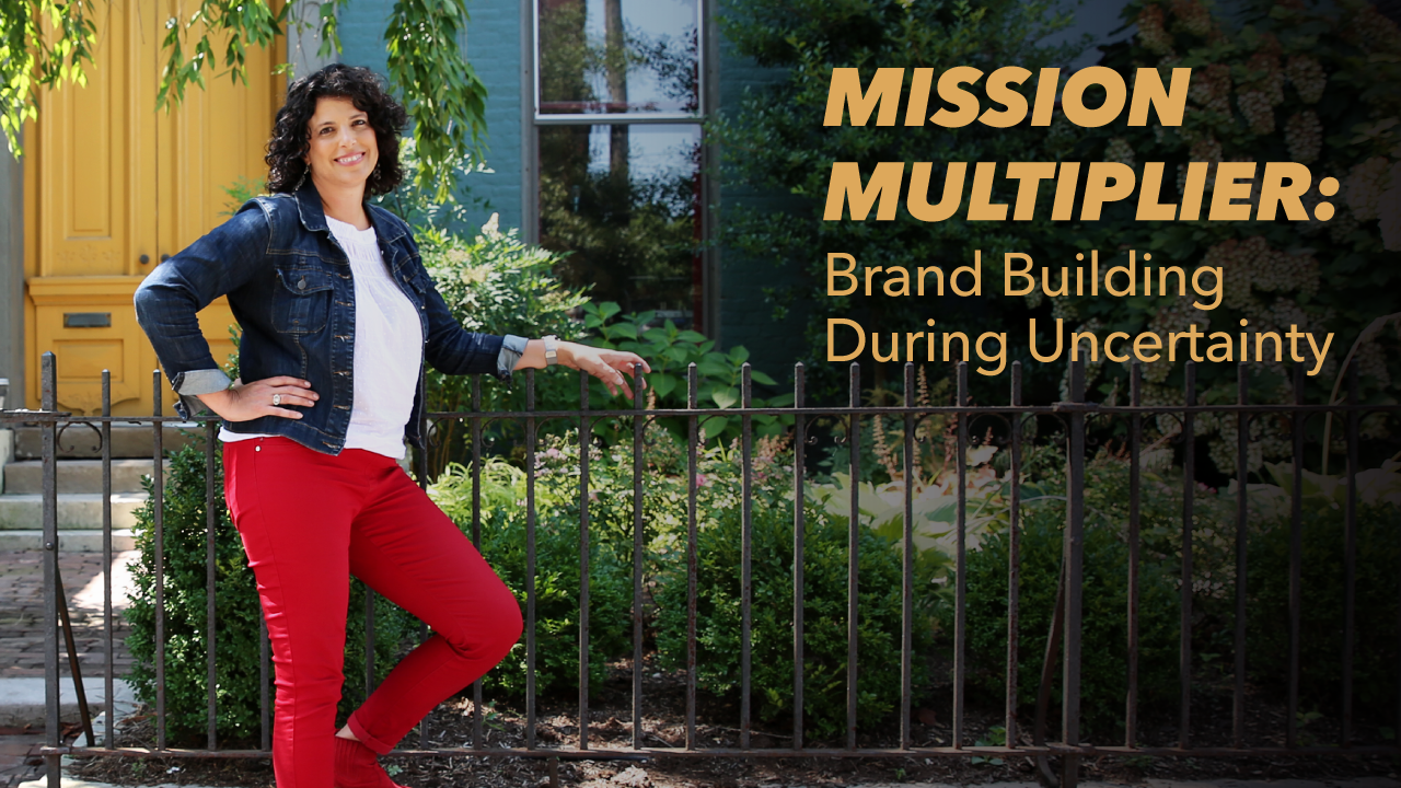 A woman in red pants and a denim jacket stands smiling by a black fence. Text reads: MISSION MULTIPLIER: Brand Building During Uncertainty. A yellow door and greenery are in the background.