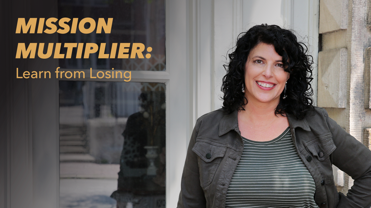 A woman with curly dark hair smiles while standing outside near a building. Text on the image reads: MISSION MULTIPLIER: Learn from Losing.