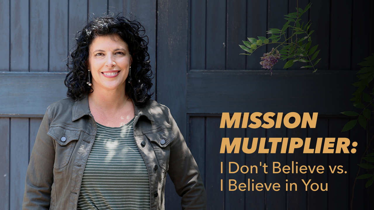 A smiling woman with curly dark hair stands in front of dark wooden doors. The text next to her reads: Mission Multiplier: I Dont Believe vs. I Believe in You. Green leaves are visible in the corner.