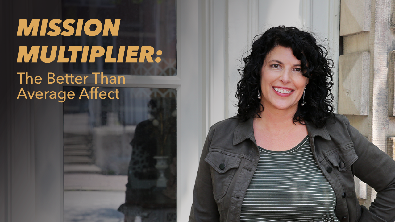 A woman with curly dark hair, wearing a striped shirt and jacket, smiles while standing with one hand on her hip next to a building. Text beside her reads, MISSION MULTIPLIER: The Better Than Average Affect.