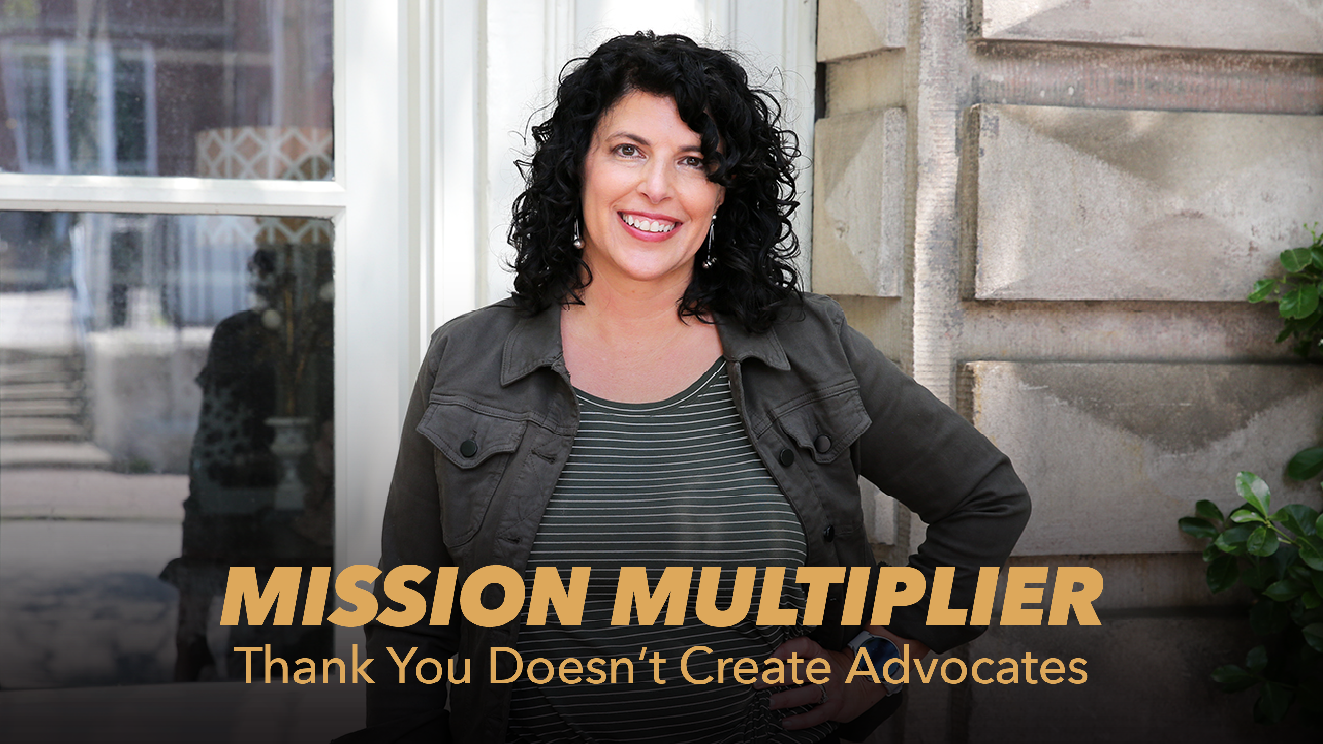 A woman with curly dark hair stands smiling with her hand on her hip in front of a building. Text on image reads: “MISSION MULTIPLIER. Thank You Doesn’t Create Advocates.”.