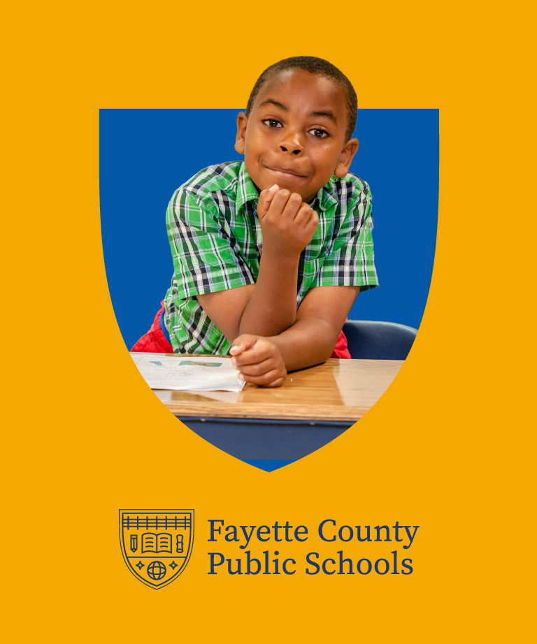 A young boy in a green plaid shirt sits at a desk, smiling and leaning on his arm. The image is framed by a blue and gold shield, with the Fayette County Public Schools logo and name underneath.