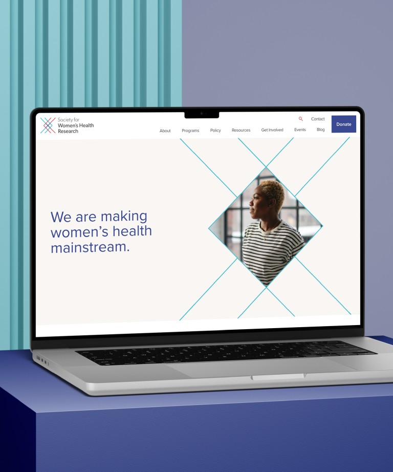 A laptop on a blue and purple surface displays a website reading “We are making women’s health mainstream,” with a photo of a person looking to the side. The background has light blue vertical lines.