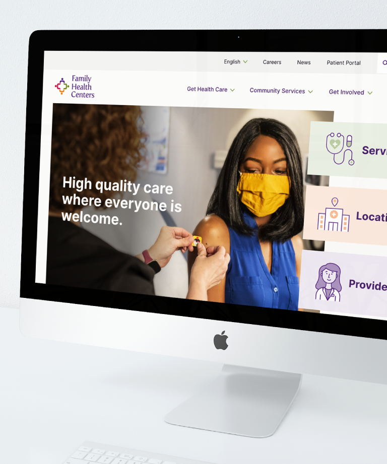 A computer screen displays the Family Health Centers website, showing a woman in a yellow mask receiving a vaccine and a message that reads, High quality care where everyone is welcome.